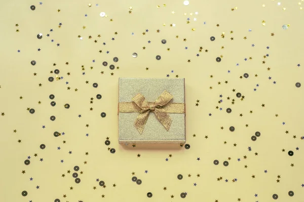 Gift in golden box on yellow background with confetti. Holidays concept. Top view, flat lay.