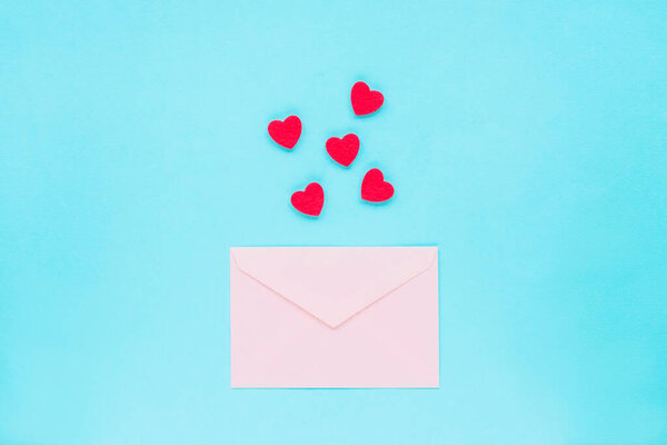 Розовый конверт и красные сердечки на синем фоне, вид сверху, плоский уголок. Концепция Дня Святого Валентина, 14 февраля.