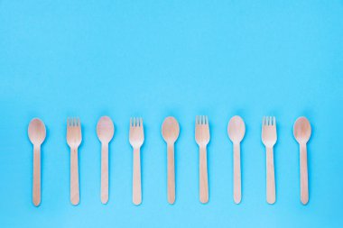 Tek kullanımlık bambu kaşıklar ve çatallar mavi arka planda. Sıfır atık. Üst görünüm, düz görünüm, kopyalama alanı.