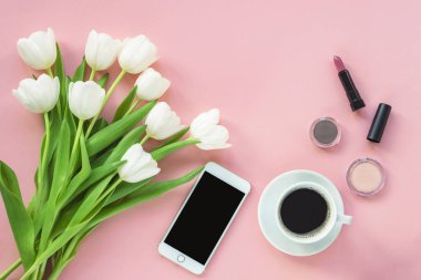 Bir fincan kahve, telefon, kozmetik ve pembe arka planda bir buket lale. Kadınlar Günü mü Anneler Günü konsepti mi?