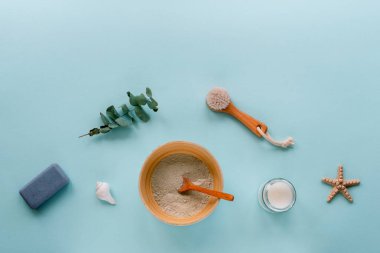 Doğal organik kozmetik ürünleri: kil, yüz fırçası, sabun, mum ve açık mavi arka planda okaliptüs yapraklı kase. Ev spa konsepti. Üst görünüm, düz görünüm, kopyalama alanı.