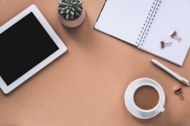Tablet bilgisayarı, not defteri, kalem, kahve fincanı ve bej arka planda sulu bitki olan bir iş yeri. Üst görünüm, düz görünüm, kopyalama alanı.