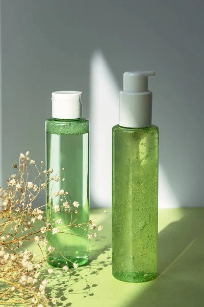 Green cosmetic bottles with face washing gel and tonic on green table. Dry gypsophila flowers decoration. Natural organic cosmetics concept
