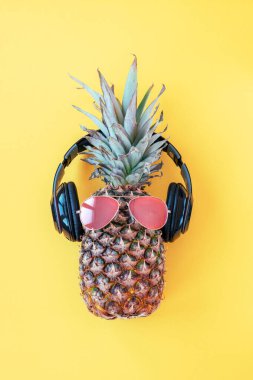 Güneş gözlüklü ananas hippisi ve sarı arka planda kulaklık. Yaz kavramı. Üst manzara, düz uzanma