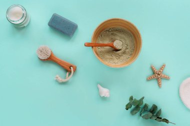 Doğal organik kozmetik ürünleri: kil, yüz fırçası, sabun, mum ve açık mavi arka planda okaliptüs yapraklı kase. Ev spa konsepti. Üst görünüm, düz görünüm, kopyalama alanı