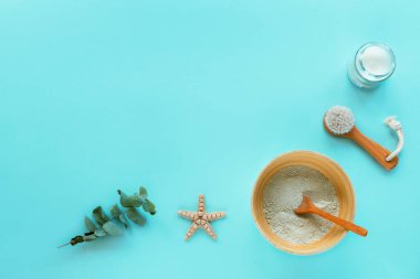 Doğal organik kozmetik ürünleri: kil, yüz fırçası, mum ve açık mavi arka planda okaliptüs yapraklı kase. Ev spa konsepti. Üst görünüm, düz görünüm, kopyalama alanı