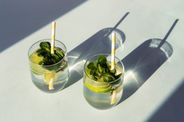 Mavi masada pipetli iki mojito. Soğuk, ferahlatıcı içecekler. Uzun, sert gölgeler, üst manzara.