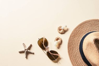 Tarafsız bir zeminde kadınların yaz aksesuarlarıyla yatıyordu. Güneş gözlüğü, hasır şapka, küpe ve denizyıldızı. Yaz yolculuğu konsepti. Üst görünüm, alanı kopyala