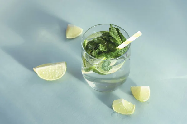 Mojito drink with straw on blue table. Cold refreshing drink with mint and lemon slices, top view.