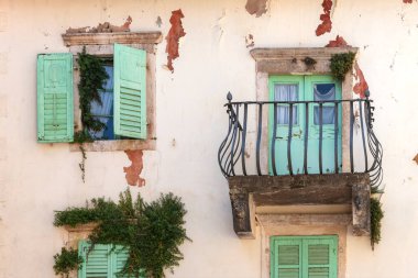 Facade of old shabby building with green shutters and balcony.