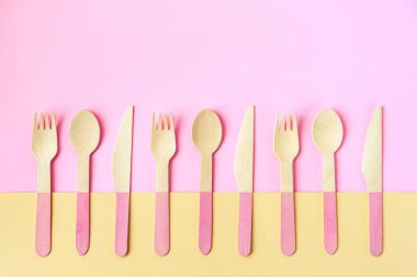 Sarı ve pembe arka planda tek kullanımlık bambu kaşıklar, çatallar ve bıçaklar. Sıfır atık. Üst görünüm, alanı kopyala.
