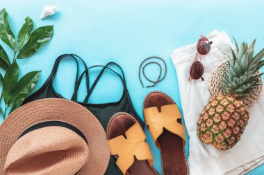 Kadınların yaz kıyafetleri, aksesuarlar, terlikler ve mavi arka planda ananas. Güzellik, moda, yaz tatili konsepti. Üst görünüm, düz görünüm, kopyalama alanı