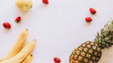 Beyaz ahşap masada ananas, muz, limon ve çilek, fotokopi alanı, üst manzara. Düz yatıyordu