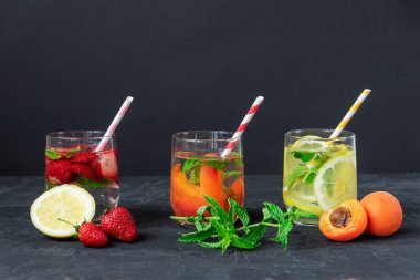 Üç farklı yaz içkisi, siyah arka planda saman olan bardakta limonata. Kapat.