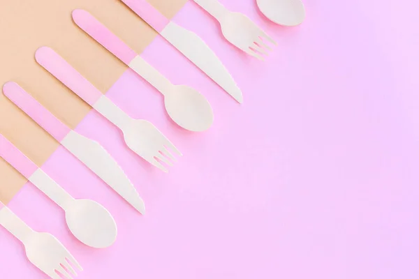 Disposable bamboo spoons, forks and knives on beige and pink background. Zero waste concept. Top view, copy space