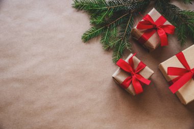 Noel ve Yeni Yıl tatili geçmişi. Noel ağacı dalları, el işi kağıdında kırmızı kurdeleli hediye kutuları. Üst görünüm, düz görünüm, kopyalama alanı.