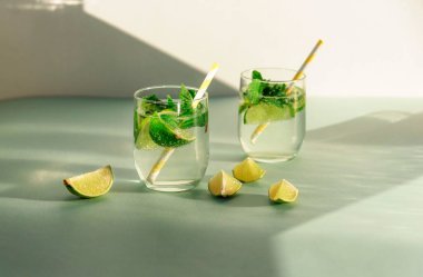 Mavi masada saman ve limon dilimli iki bardak limonata. Güneş ışığı altında soğuk, ferahlatıcı içecekler.