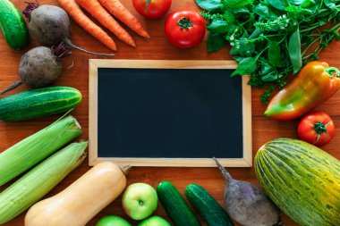 Çerçeve şeklinde organik taze sebzeler ve ortasında temiz bir karatahta. Tahta arka planda sağlıklı vegan çiğ yiyeceği. Üst görünüm, düz görünüm, maket.