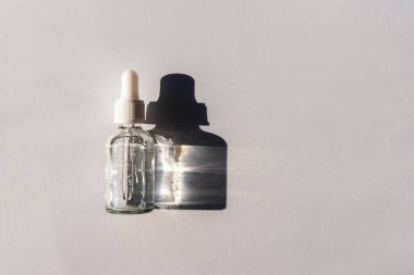 Açık gri arka planda, sert gölgeli bir şişe doğal cilt losyonu. Moda kişisel bakım ürünleri. Üst manzara, düz uzanma.