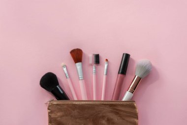 Makyaj fırçası koleksiyonu ve pembe arka planda altın kozmetik çantada ruj. Güzellik, moda konsepti. Üst manzara, düz uzanma.