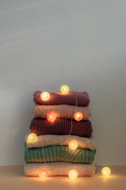 Ilık örülmüş kadın kazağı yığını. Çelenk ışıkları süslemeleri. Kış tatili kavramı.