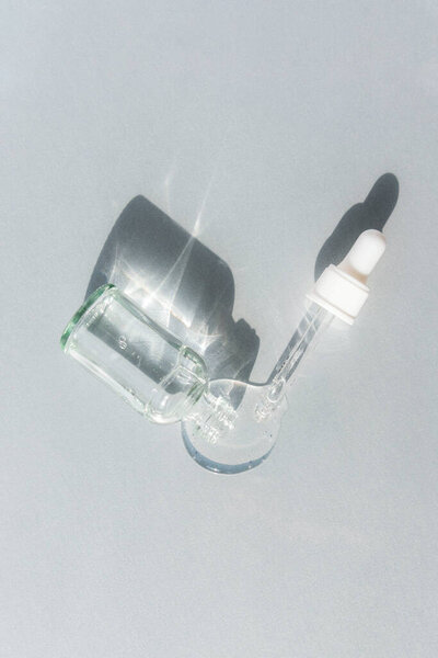 Bottle of cosmetic serum with pipette on grey background, harsh shadows. Trendy selfcare products. Top view, flat lay.