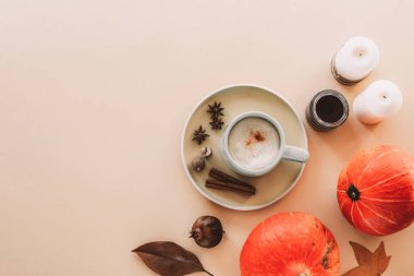 Baharatlar, mumlar ve turuncu hokkaido balkabaklarıyla kaplı bir tabak kabaklı latte. Tarafsız şeftali arka planda sonbahar yaprakları. Üst görünüm, düz görünüm, kopyalama alanı