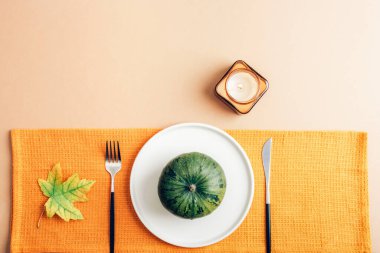 Beyaz tabakta yeşil balkabağı, bej arka planda mum ve sonbahar yaprakları mevsimlik rahat yemek konsepti. Üst manzara, düz uzanma.