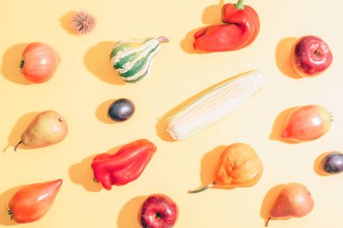 Different vegetables on light yellow background with shadows. Pumpkins, corn, bell peppers, tomatoes, pears and apples as autumn harvest concept. Top view.