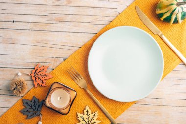 Tabak, balkabağı, mum, yapraklar ve ahşap yüzeyde sarı peçeteyle zarif bir sonbahar masa düzenlemesi. Üst görünüm, düz görünüm, model.