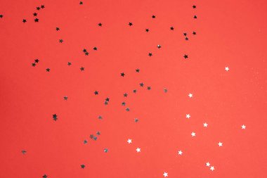 Kırmızı arka planda parıldayan yıldız şeklinde konfeti. Bayram kutlaması konsepti. Üst görünüm.