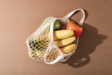 Assorted fruits placed in a mesh bag on a warm surface showing a simple natural food arrangement with light and shadows. Top view.