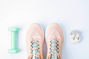 Pembe koşu ayakkabıları, dambıl ve beyaz arka planda kablosuz kulaklık. Spor ve sağlıklı yaşam tarzı kavramı. Üst manzara, düz uzanma.