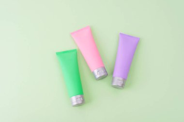 Pastel çok renkli kozmetik tüpleri yeşil arka planda. Güzellik damgası için çok az cilt bakımı. Üst görünüm, model.