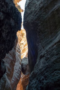 Dik taş duvarları ve yukarıdan gelen güneş ışığı olan dar kayalık kanyon. Kıbrıs adasında Avakas Vadisi Kanyonu.