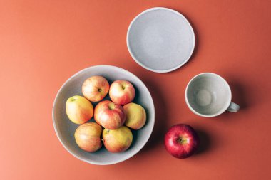 Bir kasede taze elmalar ve kahverengi arka planda fincan tabağı olan boş bardaklar. Üst manzara, düz uzanma.