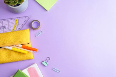 School supplies, notepad, yellow pencil-case, pencil, ruler, succulent plant and paper clips on purple background. Top view, flat lay, copy space.