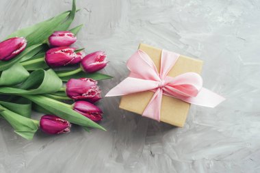 Pembe kurdeleli hediye kutusu ve açık gri renkli arka planda pembe laleler. Kadınlar Günü, Sevgililer Günü konsepti. Üst görünüm.