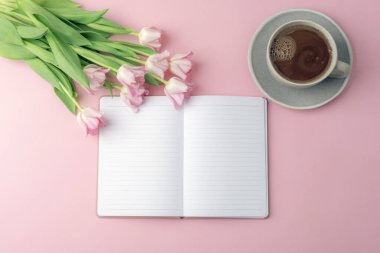 Açık defter ve pembe arka planda kahve fincanı olan pembe laleler. Sıcak bir bahar sabahı, Anneler Günü konsepti. Üst manzara, düz uzanma.