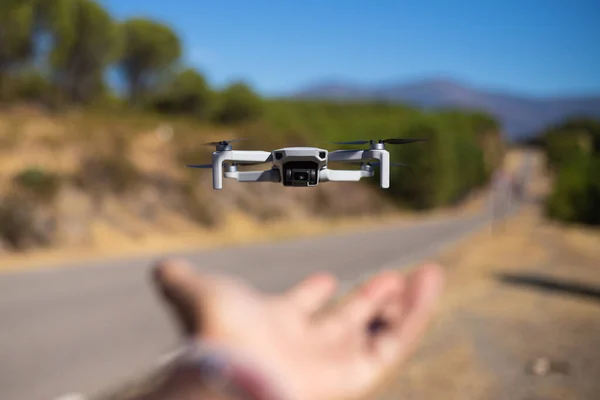 Hand grabbing a flying drone outdoors next to a road with trees in the background