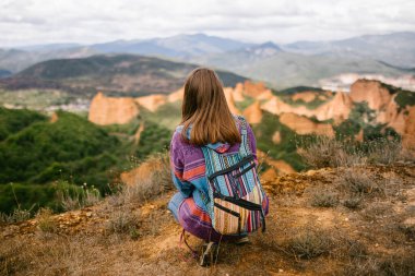 Tanımlanamayan yürüyüşçü kadın yere oturmuş dağ manzarasına bakıyor.