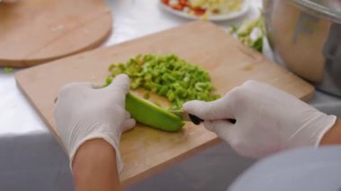 Usta aşçı, ahşap kesim tahtasına taze yeşil dolma biber hazırlar. Titizlikle dilimleme tekniklerini ve ilgi çekici mutfak sahnesinin renkli malzemelerini vurgular.