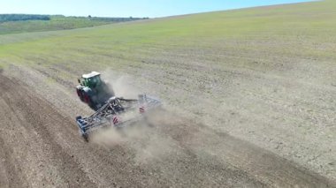 Tarım traktörü geniş alandaki toprağı aktif olarak sürüyor, toz bulutlarıyla çiftçiliğin özünü yakalıyor ve makinelerin verimliliğini ve gücünü gösteriyor.