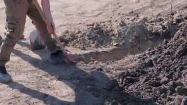 İşçi aktif olarak kürekle bir kanal kazıyor, görevin ilerleyişini ve toprağın dokusunu yakalıyor, inşaat çalışmalarını vurguluyor