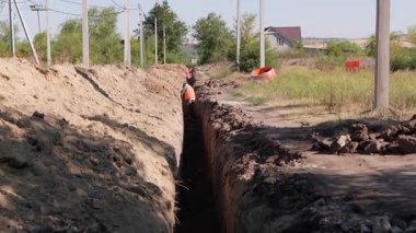 Güvenlik donanımlı inşaat işçileri su veya kanalizasyon sistemi genişlemesi için aktif bir siper kazarak, işbirlikçi çaba ve altyapı gelişimindeki ilerlemeyi vurguluyorlar.