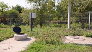 Sıralı çerçeveler çimenli bir alanda açık bir rögar kapağını tasvir ederek kanalizasyon sistemlerinin ve çevreleyen doğal çevrenin süregelen bakımını vurguluyor.