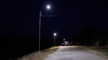 Akıllı sokak lambaları gece parlıyor, sakin bir yol boyunca güneş enerjisi özelliklerini vurguluyor, güvenlik ve çevre dostu kentsel aydınlatma çözümlerini destekliyor