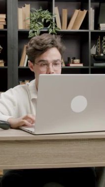 Modern bir ofiste internetli bir dizüstü bilgisayarın önünde çalışan genç bir serbest çalışan. Bilgisayarda daktilo eden ve müşterilerle uzaktan çalışan gözlüklü yakışıklı bir adam.