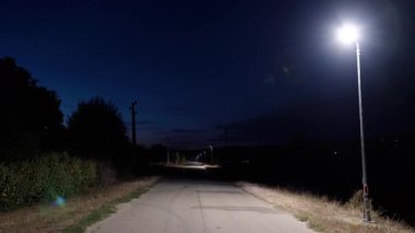 Parlak ışıklarla aydınlatılmış, yeşil ve açık gökyüzü ile kaplı sakin ve davetkar bir atmosfer yaratan sakin bir yol.