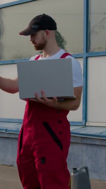 Kırmızı tulumlu erkek otomobil teknisyeni arabanın havalandırma sistemini dizüstü bilgisayarla teşhis ediyor, kaputu açık aracın yanında duruyor, teknik uzmanlık ve profesyonellik gösteriyor.